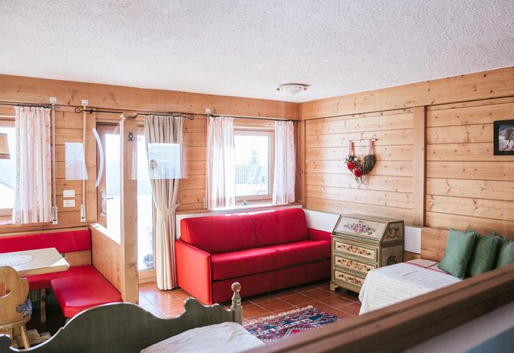 Familienzimmer mit Holzwänden, rotem Sofa, Essecke und mehreren Betten