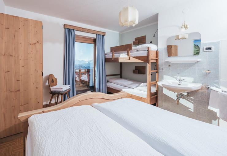 Hüttenzimmer mit Waschbecken, Doppelbett, Stockbett und Balkon