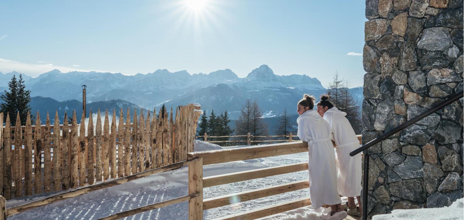 A couple in white bathrobes outdoors with a view of the winter mountain scenery