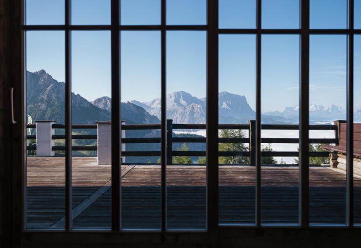 Vista attraverso una finestra su una terrazza in legno con panorama montano delle Dolomiti.