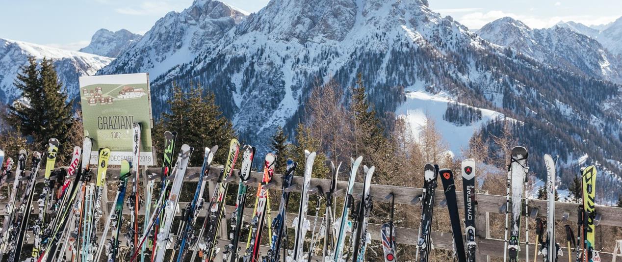 Skis leaning against a wooden fence with snow-covered mountains in the background.