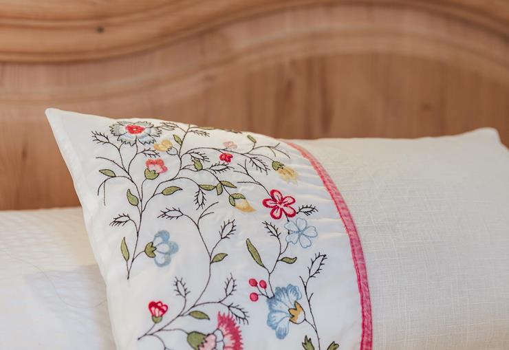 Nahaufnahme eines mit Blumen bestickten Kissens auf einem Doppelbett