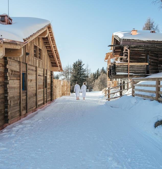 Snow-covered path between wooden chalets with two people in bathrobes
