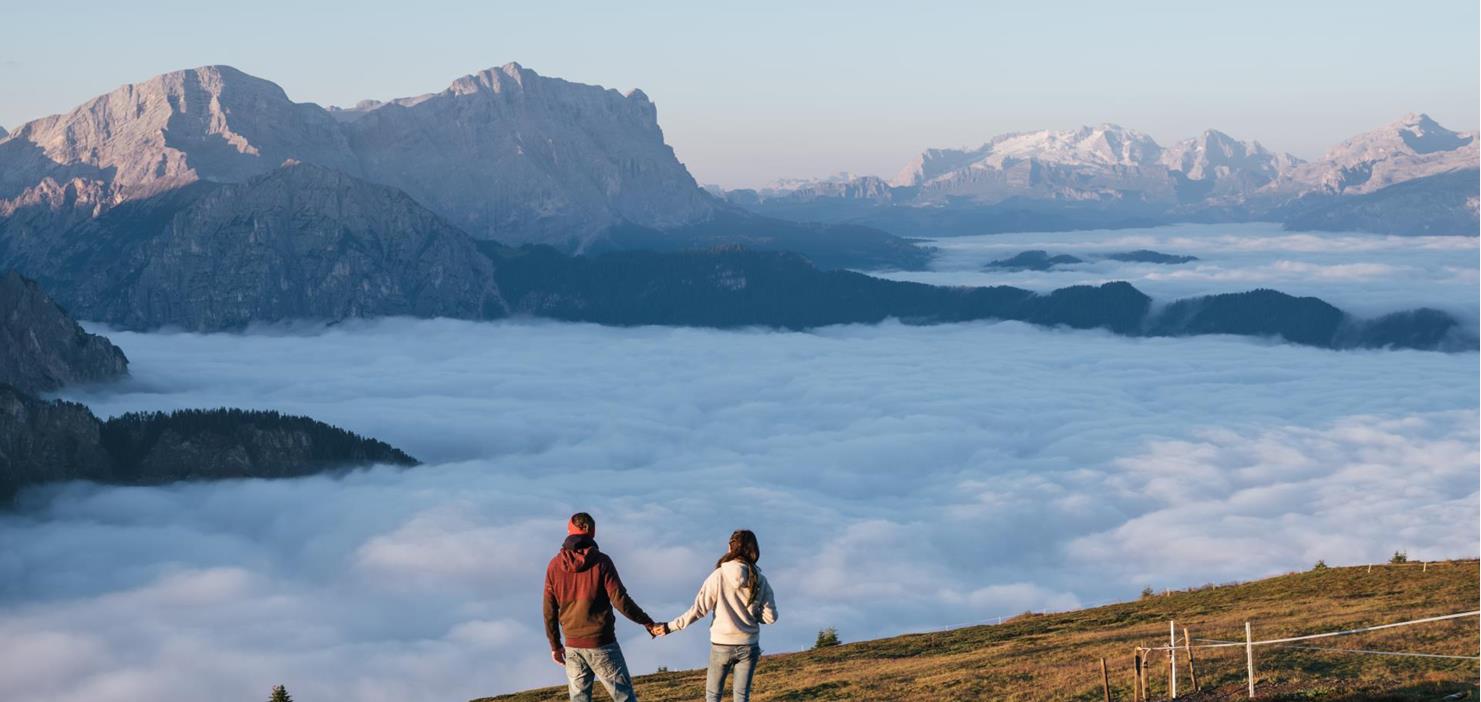 A couple on an alpine meadow, with fog and mountains in the background.