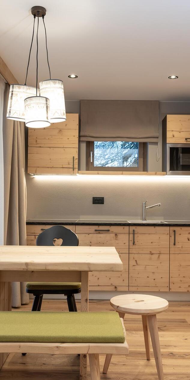 Essbereich der Ciasa Rosina mit Holztisch, grüner Sitzbank und heller Küchenzeile