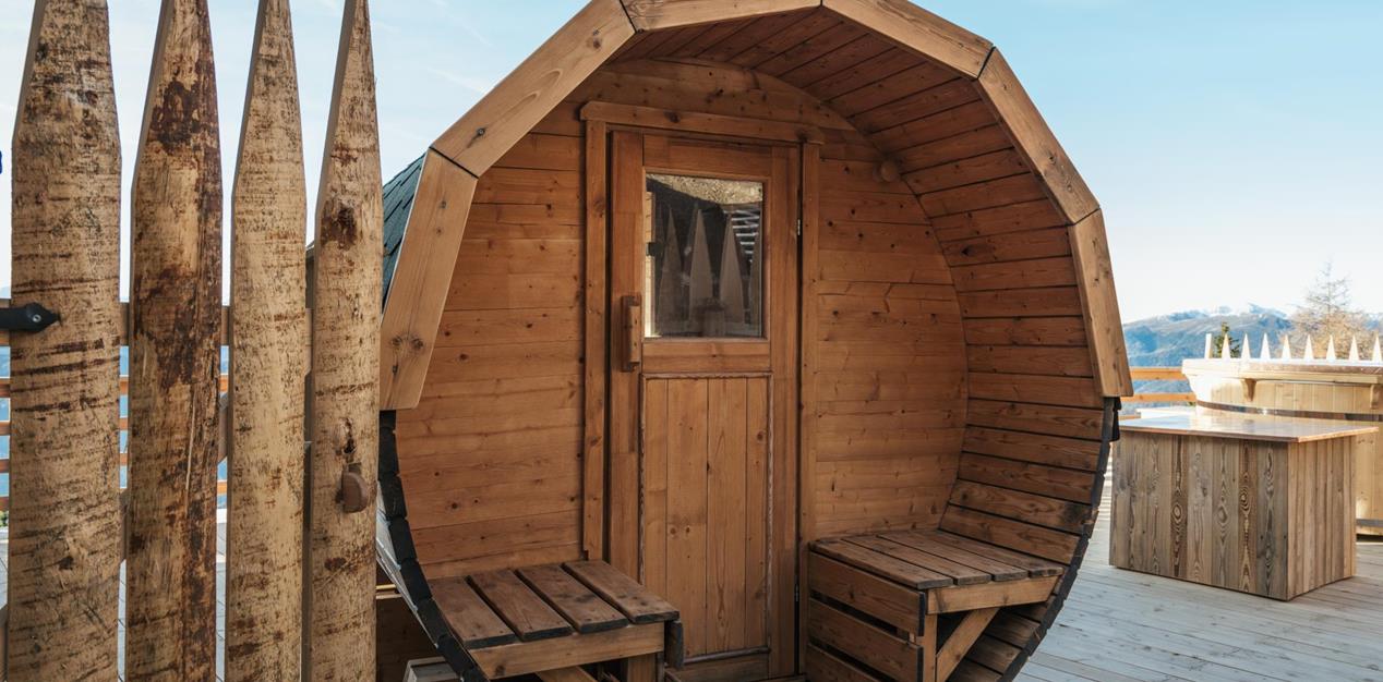 Sauna-Fass mit Whirlpool im Hintergrund.