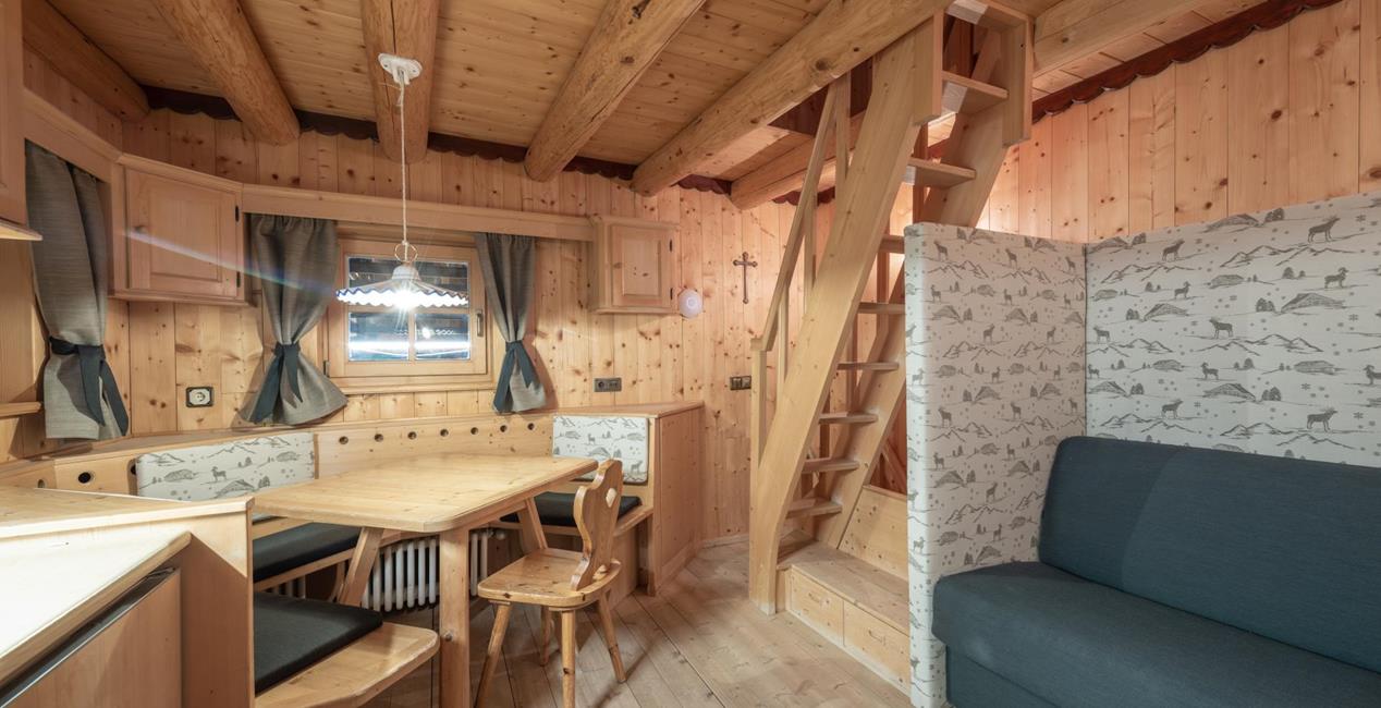Living and dining area of Ciasa Vedla with wooden table, corner bench, blue sofa and stairs to the sleeping loft