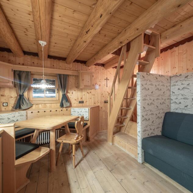Wohn- und Essbereich der Ciasa Vedla mit Holztisch, Eckbank, blauem Sofa und Treppe zur Schlafgalerie