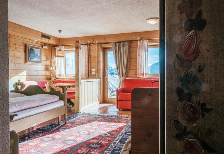 Familienzimmer mit Holzwänden, rotem Sofa, Sitzecke, Bett und Balkonblick auf die Berge