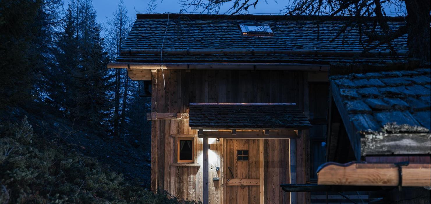 Casa in legno Ciasa Arnika nel bosco al crepuscolo con ingresso illuminato