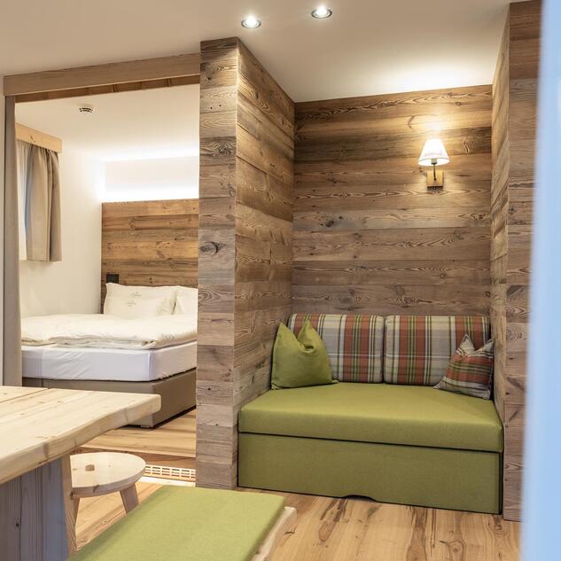 Wohnbereich der Ciasa Rosina mit Holzwänden, Sitzecke und Blick ins Schlafzimmer
