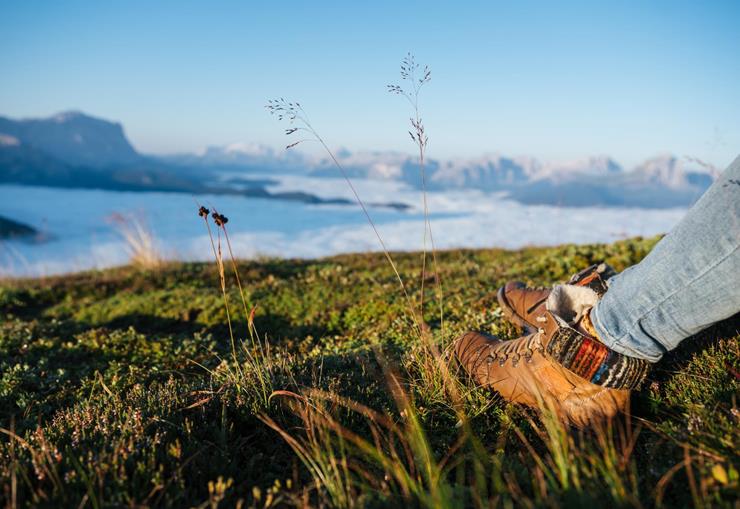 Hiking boots on an alpine meadow with views of the Dolomites and a sea of clouds.