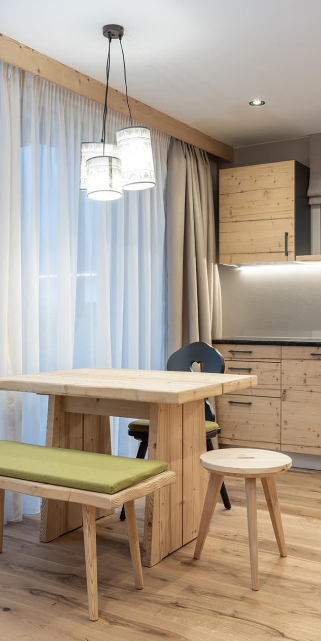 Essbereich der Ciasa Rosina mit Holztisch, grüner Sitzbank und heller Küchenzeile
