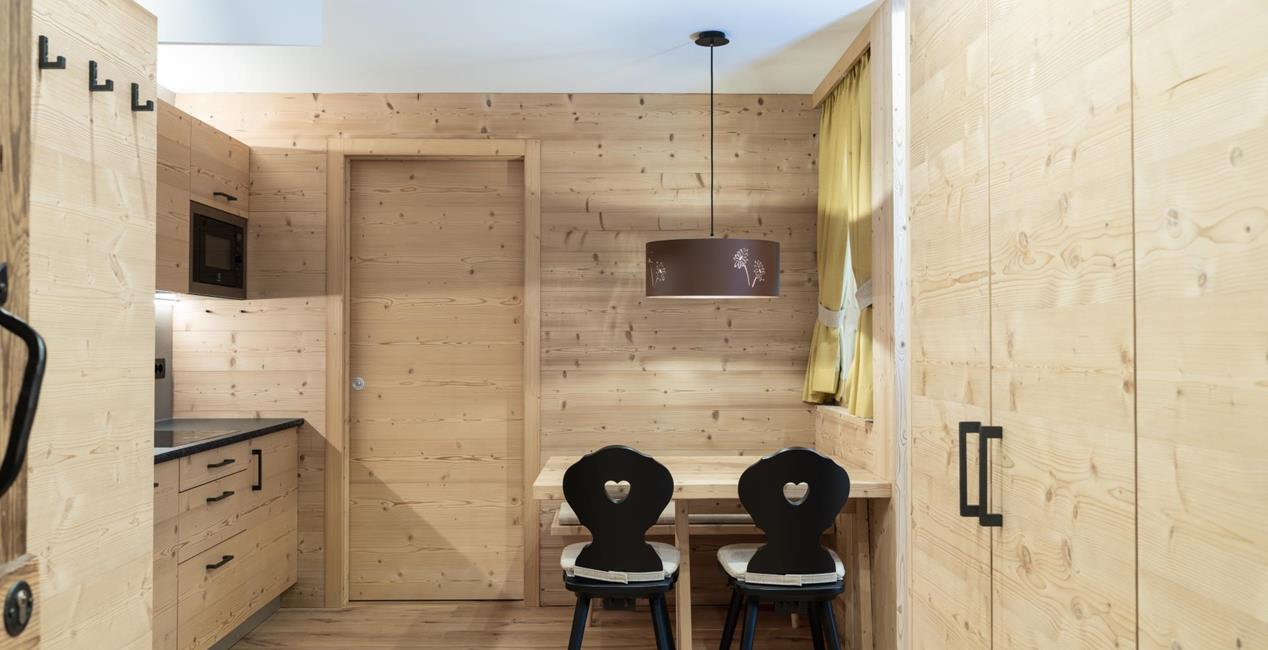 Living area of Ciasa Arnica with light wood furniture, seating and kitchen