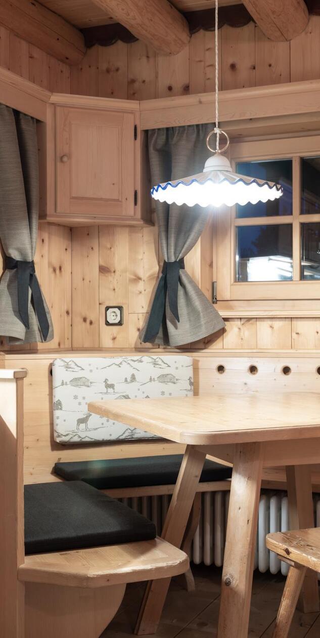 Wohn- und Essbereich der Ciasa Vedla mit Holzwänden, Eckbank, Holztisch und Küchenzeile