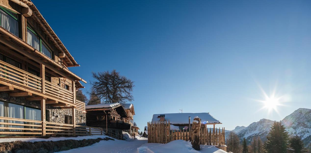 Holzchalets in verschneiter Winterlandschaft im Sonnenschein.