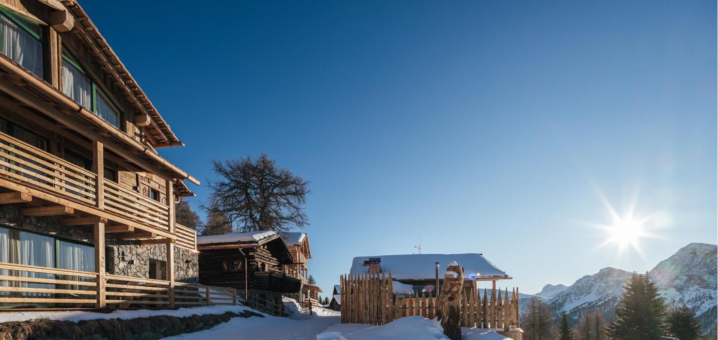 Wooden chalets in a sunlit, snow-covered winter landscape.
