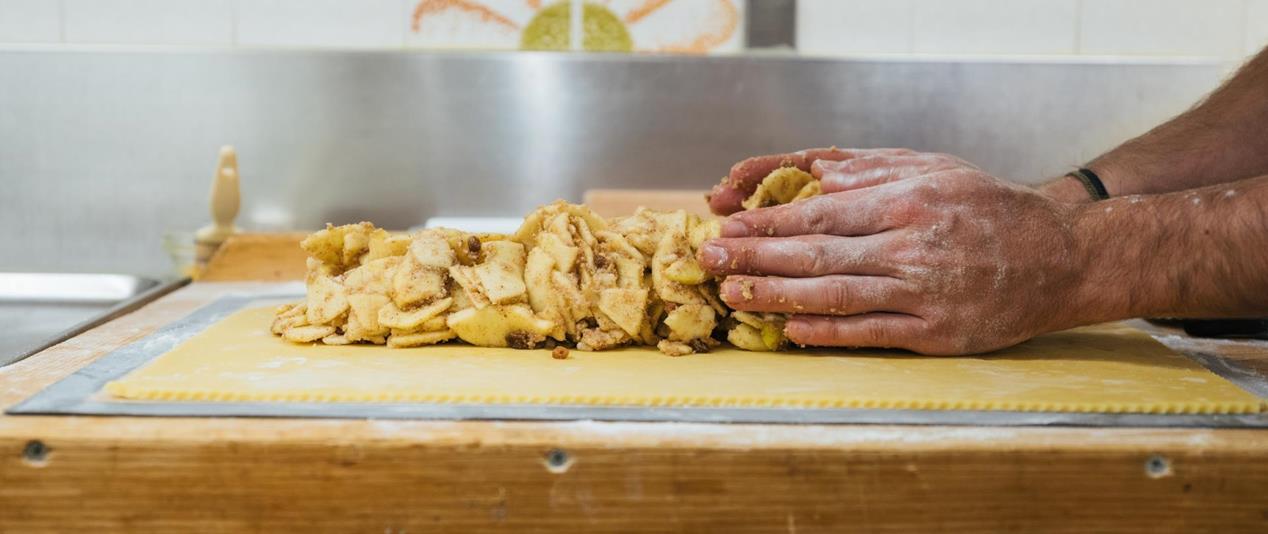 Mani che distribuiscono pezzetti di mela su un impasto.