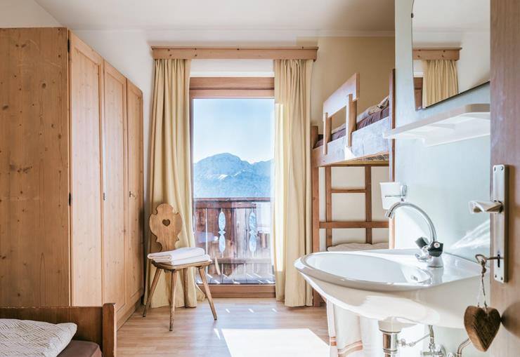 Hüttenzimmer mit Waschbecken, Stockbett, Holzschrank und Balkonblick auf die Berge